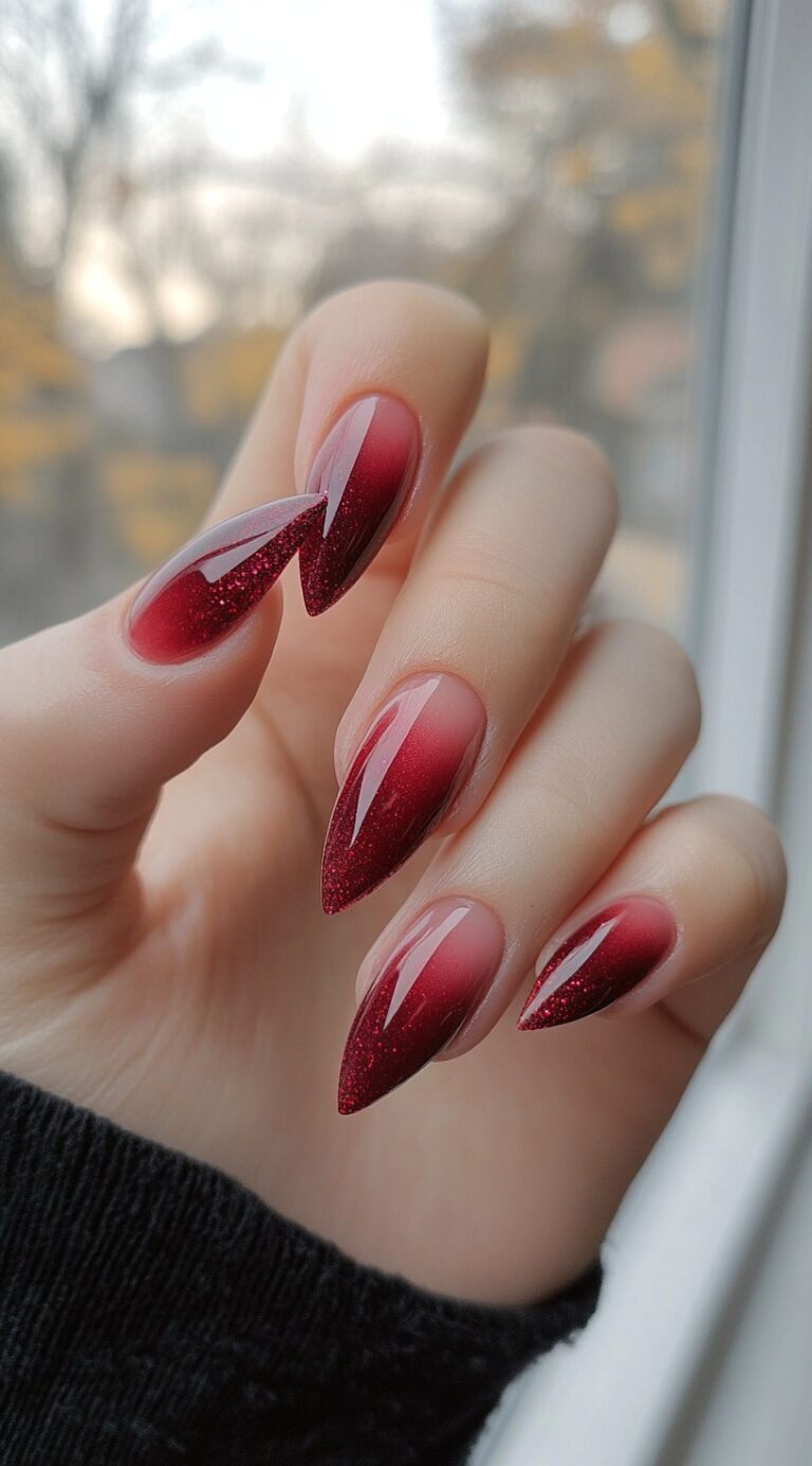 Long almond nails with a smooth red ombre fade and subtle red glitter that catches the light.