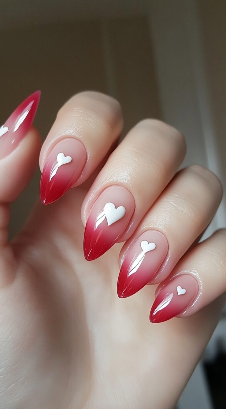 Long almond-shaped nails with a soft red ombre fade and white heart decals on each nail.