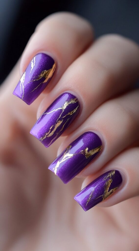 Square nails painted in metallic purple with irregular gold foil streaks resembling cracks or marble veining.