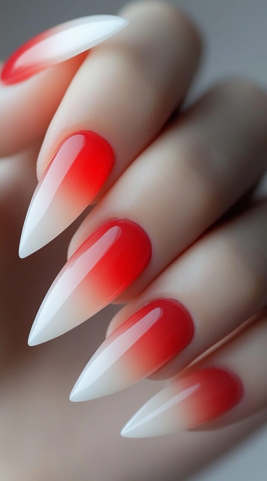 A hand with long almond-shaped acrylic nails featuring a smooth red to milky white ombre finish.