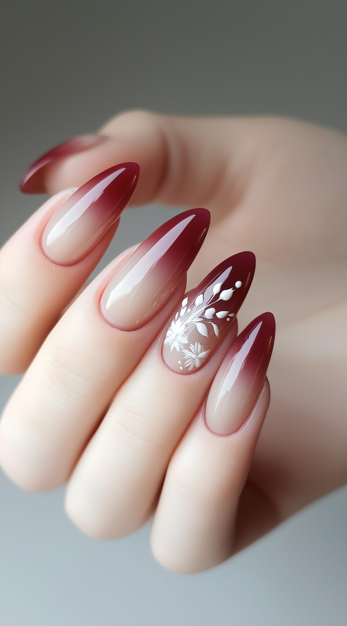 Glossy oval nails fade from nude to deep red, with one nail featuring a detailed white floral design.