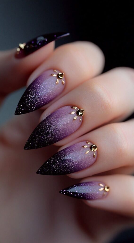 Almond-shaped nails in a gradient of purple glitter with small gold sunburst studs near the cuticles.