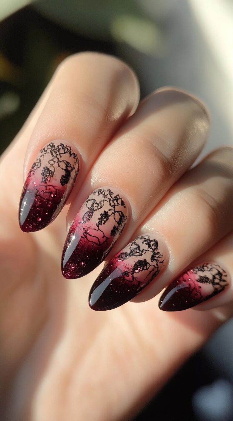 A set of almond-shaped red to black ombre nails with glitter and delicate black lace detailing at the top.